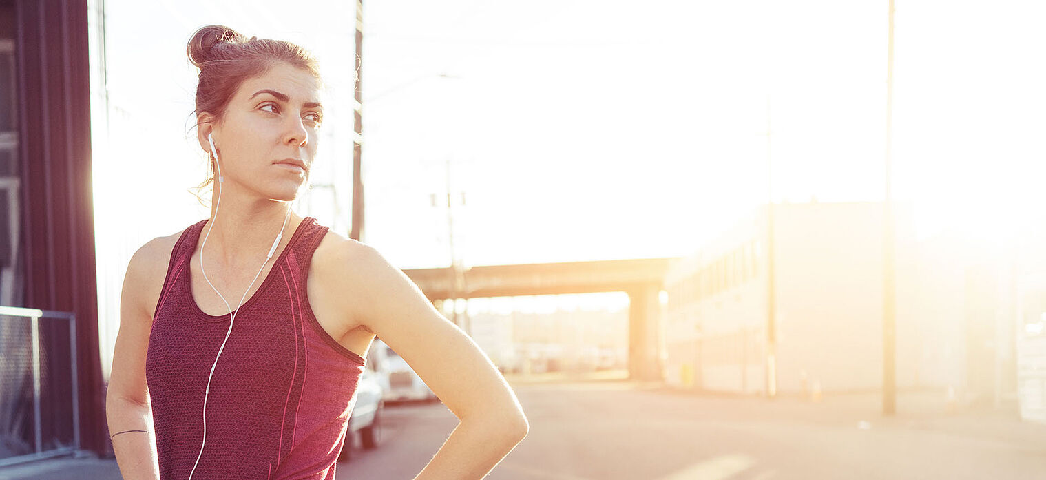 A woman in athletic gear, standing with a confident pose, possibly after a workout, with the sunlight creating a dramatic effect in the background.